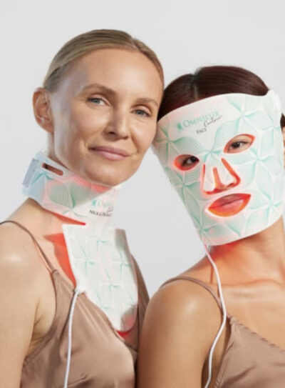 Two women side by side: On the left, one wearing the NECK and DECOLLETAGE OMNILUX CONTOUR medical grade led therapy mask, the second, on the right, wearing the Medical Grade OMNILUX CONTOUR Face mask.